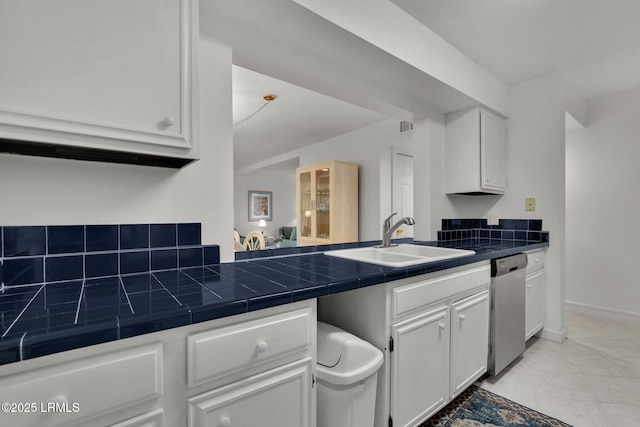 kitchen featuring sink, light tile patterned floors, dishwasher, white cabinets, and tile countertops