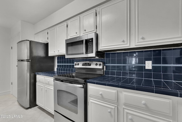 kitchen with light tile patterned floors, appliances with stainless steel finishes, tasteful backsplash, white cabinets, and tile countertops