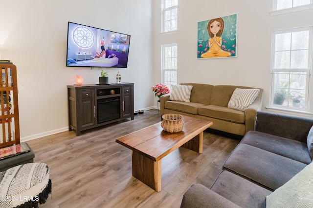 living room featuring a healthy amount of sunlight, light wood-type flooring, and a towering ceiling