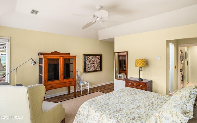 bedroom with ceiling fan, stacked washer / dryer, and wood-type flooring