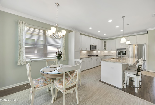 kitchen with white cabinetry, appliances with stainless steel finishes, crown molding, and decorative light fixtures