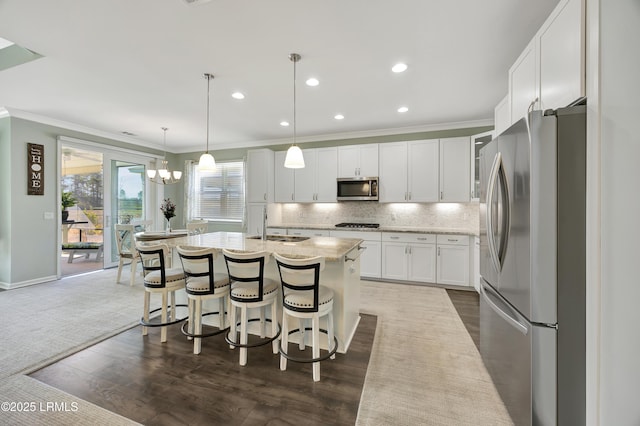 kitchen with pendant lighting, white cabinetry, appliances with stainless steel finishes, and a kitchen island with sink