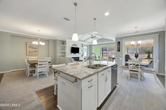 kitchen with a fireplace, white cabinetry, sink, light stone countertops, and a center island with sink