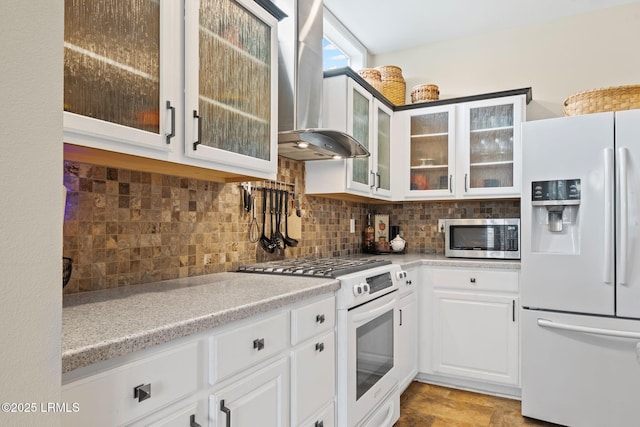 kitchen featuring tasteful backsplash, wall chimney range hood, white appliances, and white cabinets