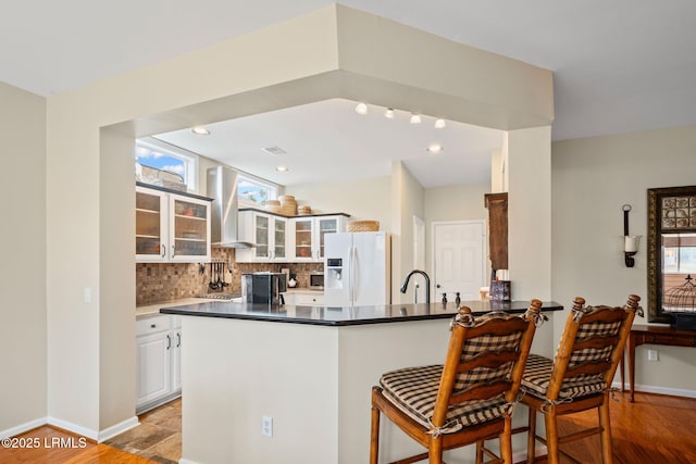 kitchen featuring range hood, white refrigerator with ice dispenser, white cabinets, and kitchen peninsula