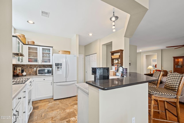 kitchen with tasteful backsplash, white cabinetry, ceiling fan, kitchen peninsula, and white appliances