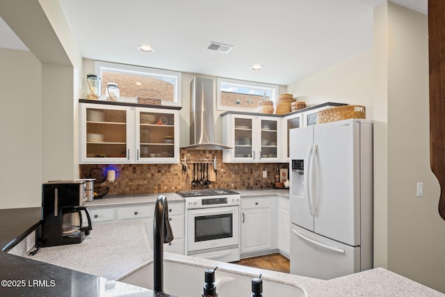 kitchen with tasteful backsplash, white cabinets, light stone counters, white appliances, and wall chimney exhaust hood