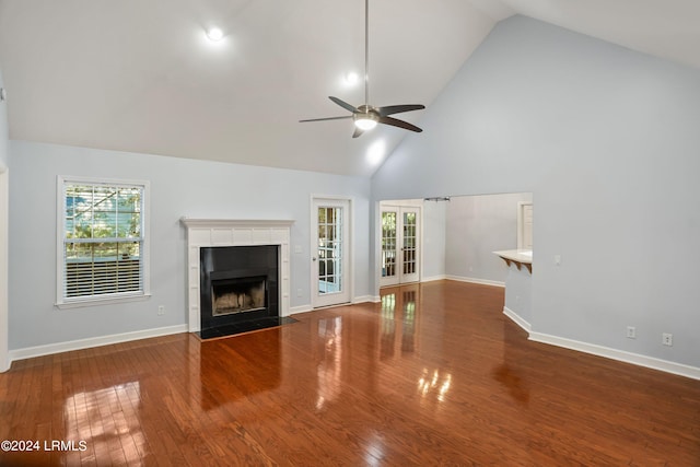 unfurnished living room featuring ceiling fan, high vaulted ceiling, a tiled fireplace, and hardwood / wood-style floors