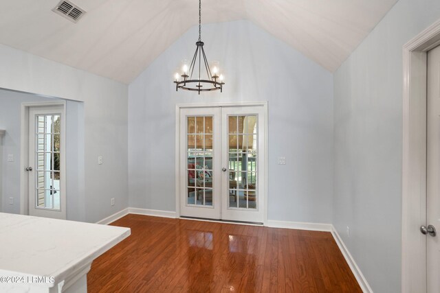 unfurnished dining area with vaulted ceiling, a notable chandelier, dark hardwood / wood-style flooring, and french doors