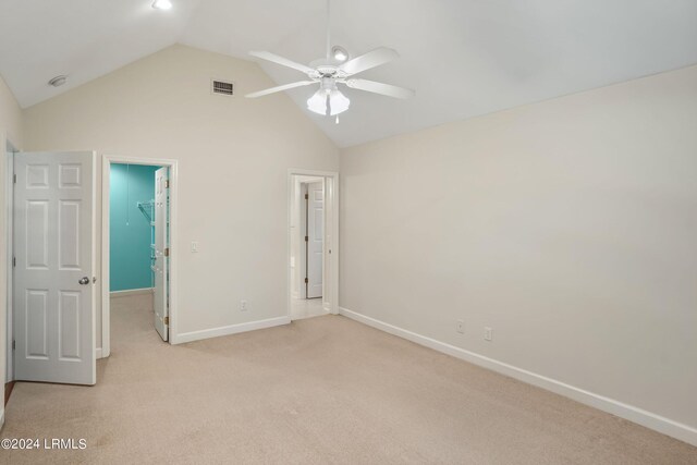 unfurnished bedroom with lofted ceiling, a spacious closet, light colored carpet, ceiling fan, and a closet