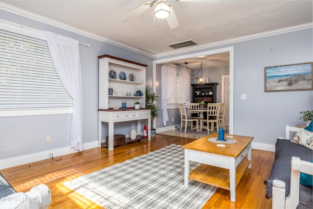 living room with a ceiling fan, baseboards, wood finished floors, visible vents, and ornamental molding