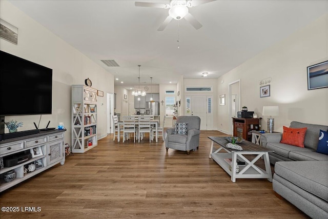 living room with ceiling fan with notable chandelier, wood finished floors, and visible vents