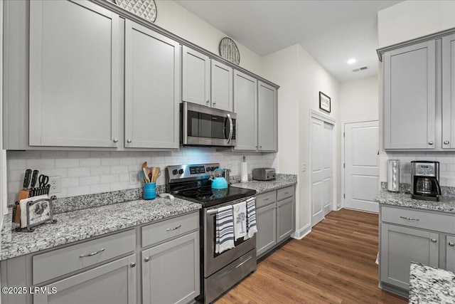 kitchen with gray cabinetry, stainless steel appliances, tasteful backsplash, light stone countertops, and dark hardwood / wood-style flooring