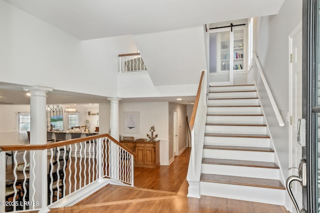 staircase featuring a high ceiling, wood finished floors, and decorative columns