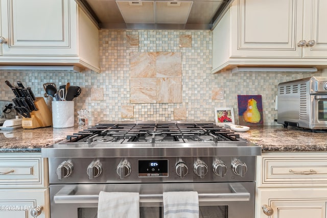 kitchen with a toaster, cream cabinets, wall chimney exhaust hood, and gas range