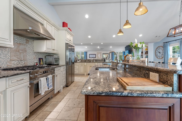 kitchen featuring appliances with stainless steel finishes, stone tile flooring, wall chimney range hood, a sink, and recessed lighting