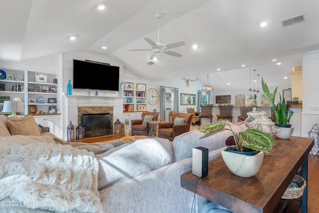 living room with ceiling fan, a fireplace, visible vents, built in features, and vaulted ceiling