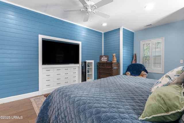 bedroom with wood walls, wood finished floors, visible vents, and baseboards