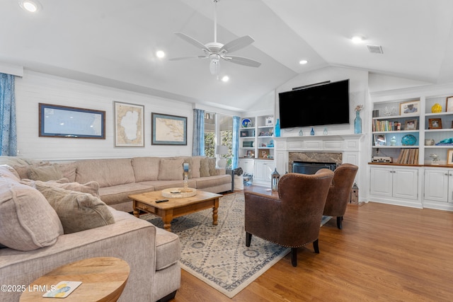 living room featuring built in features, a fireplace, visible vents, light wood-style floors, and vaulted ceiling