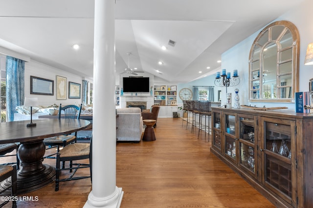 dining space with a ceiling fan, vaulted ceiling, decorative columns, and wood finished floors