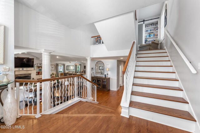 stairway with a fireplace, a towering ceiling, ornate columns, and wood finished floors