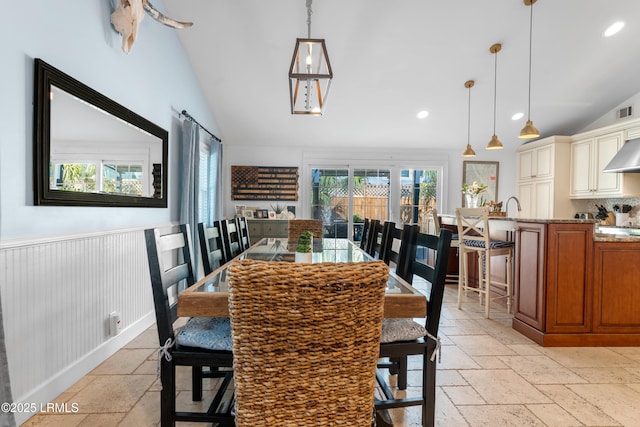 dining space with a wainscoted wall, vaulted ceiling, stone tile flooring, and recessed lighting