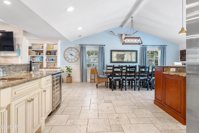 kitchen with lofted ceiling with beams, wine cooler, cream cabinets, stone counters, and stone tile flooring