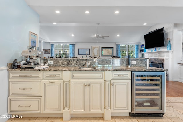 kitchen featuring beverage cooler, cream cabinetry, a sink, and light stone counters