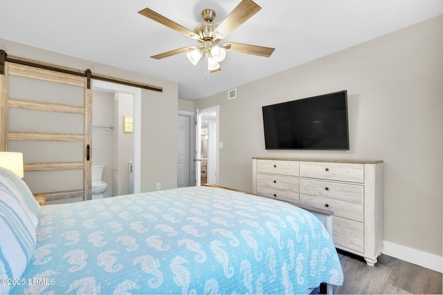 bedroom with ceiling fan, ensuite bath, a barn door, and dark hardwood / wood-style flooring