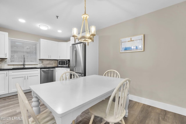 kitchen with appliances with stainless steel finishes, pendant lighting, sink, backsplash, and hardwood / wood-style flooring