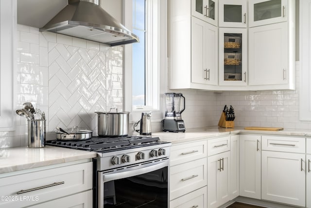 kitchen with stainless steel range with gas cooktop, wall chimney range hood, decorative backsplash, and white cabinets