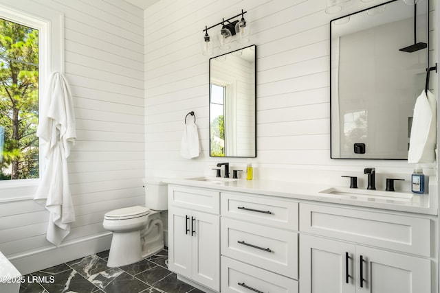 full bath with marble finish flooring, wooden walls, toilet, double vanity, and healthy amount of natural light