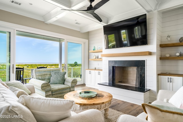 living area with light wood-type flooring, a ceiling fan, beam ceiling, a high end fireplace, and wooden walls