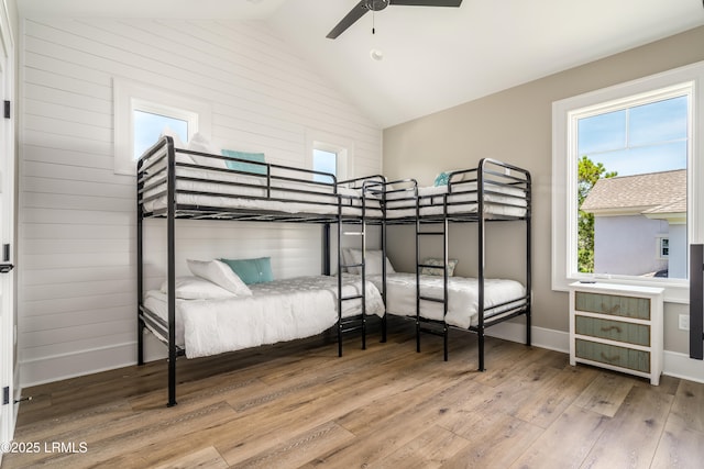 bedroom featuring wood finished floors, lofted ceiling, baseboards, ceiling fan, and wooden walls