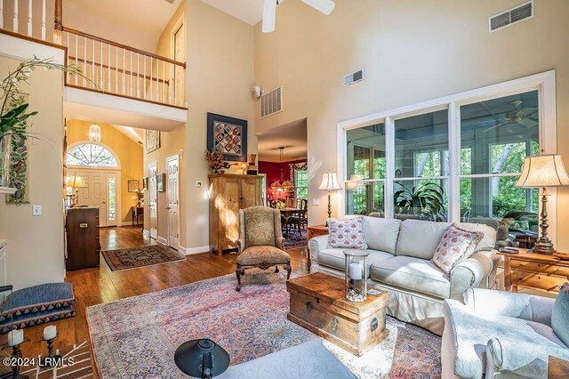 living room featuring a towering ceiling, ceiling fan with notable chandelier, and hardwood / wood-style flooring