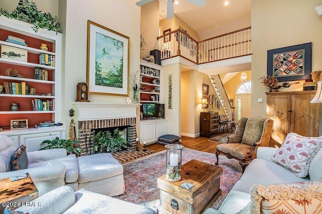 living room with built in features, a wall mounted AC, a high ceiling, a brick fireplace, and light wood-type flooring