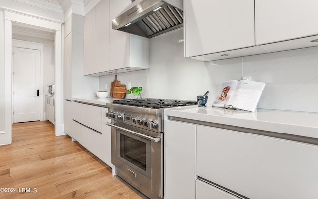 kitchen with light wood-type flooring, white cabinets, stainless steel stove, and wall chimney range hood