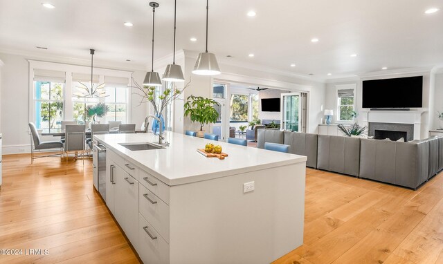 kitchen featuring decorative light fixtures, sink, a center island with sink, and white cabinets