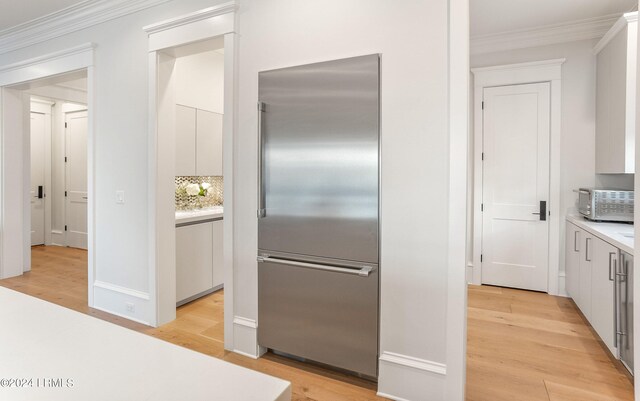 kitchen with ornamental molding, stainless steel built in fridge, light wood-type flooring, and white cabinets