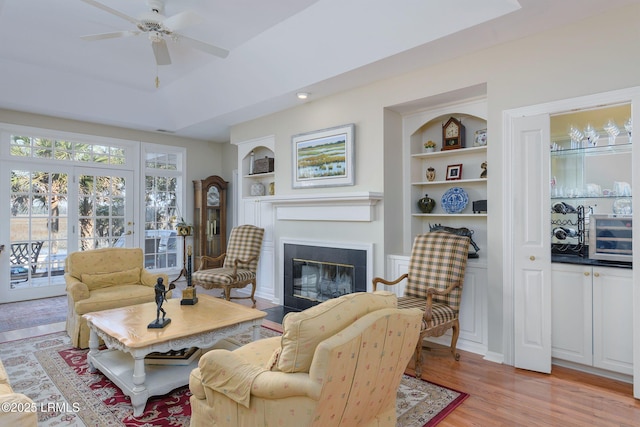 living room with built in shelves, light hardwood / wood-style floors, and ceiling fan