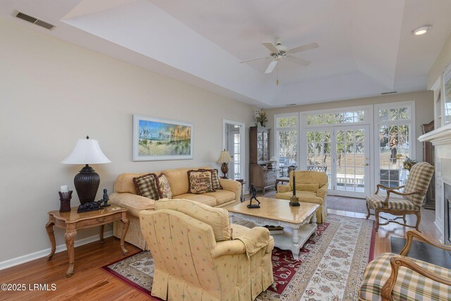 living room featuring light hardwood / wood-style flooring, a raised ceiling, and ceiling fan