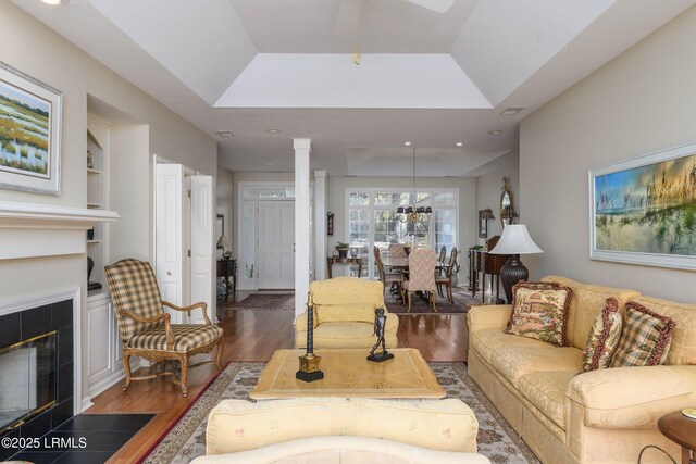 living room featuring built in features, a fireplace, decorative columns, a tray ceiling, and dark wood-type flooring