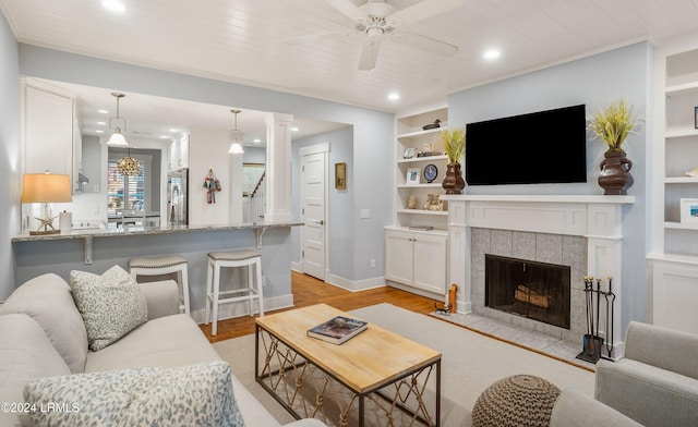 living room featuring a tile fireplace, built in features, ceiling fan, wood ceiling, and light wood-type flooring