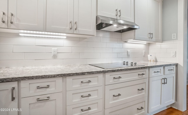 kitchen featuring light hardwood / wood-style flooring, tasteful backsplash, black electric stovetop, light stone counters, and white cabinets