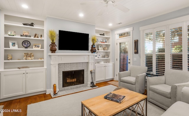 living room with built in shelves, wood ceiling, light hardwood / wood-style flooring, ceiling fan, and a fireplace