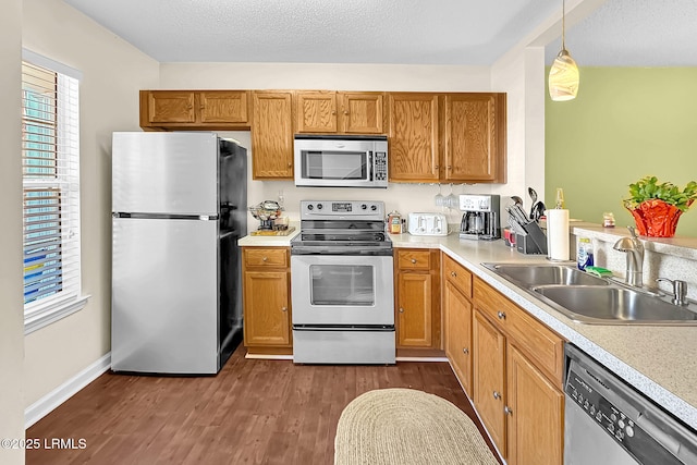 kitchen with pendant lighting, sink, stainless steel appliances, a textured ceiling, and dark hardwood / wood-style flooring