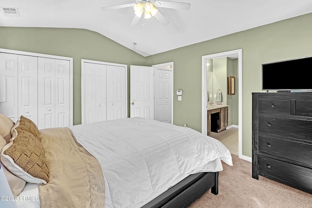 carpeted bedroom featuring vaulted ceiling, two closets, ceiling fan, and ensuite bath