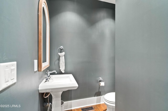 half bath featuring toilet, a sink, visible vents, wood finished floors, and baseboards