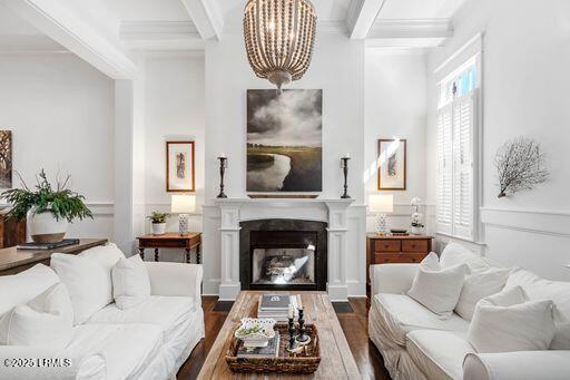 living room featuring dark wood finished floors, wainscoting, ornamental molding, a fireplace, and beam ceiling