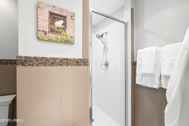 bathroom featuring toilet, a shower stall, tile walls, and wainscoting